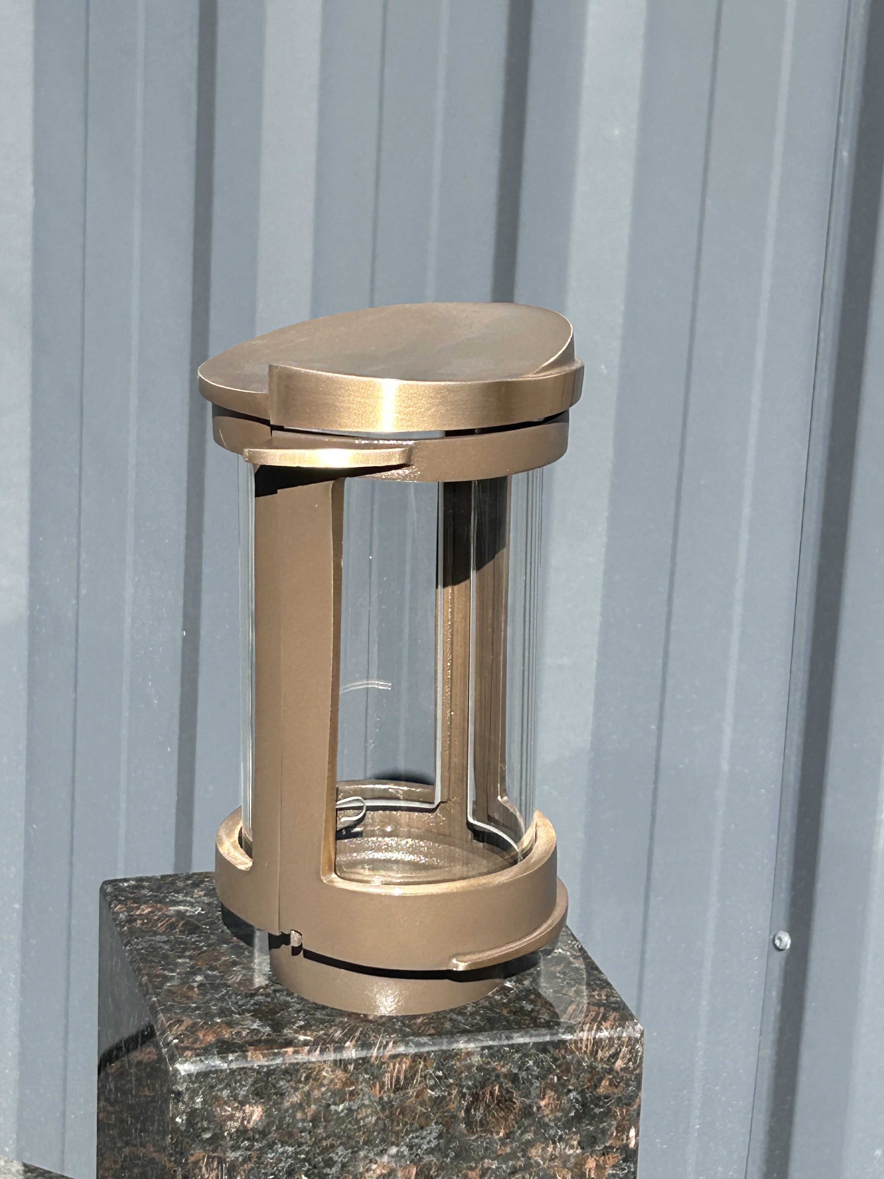 Eine bronzefarbene Laterne steht auf einem dunklen Marmorsockel vor einer grauen Wand