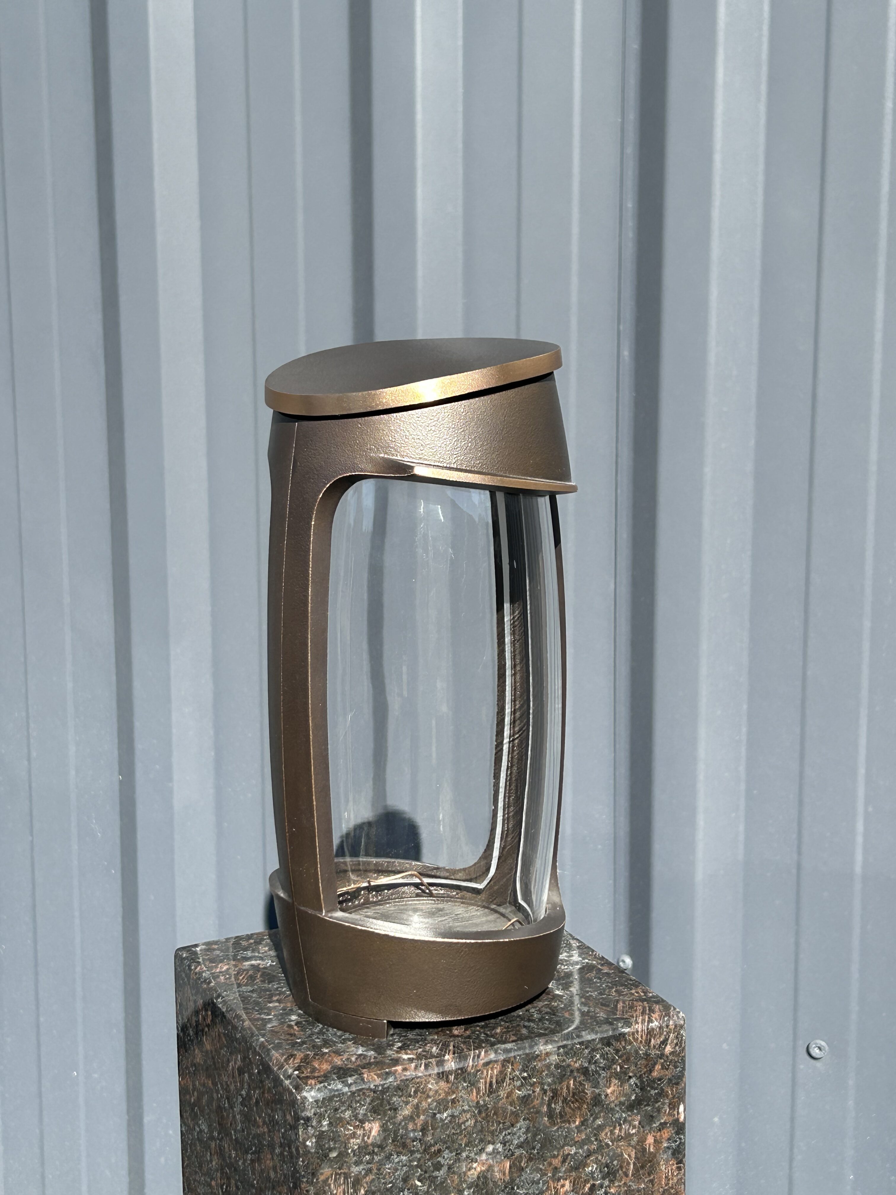 Eine moderne Kaffeepresse mit bronzefarbenem Rahmen steht auf einem Steinblock vor einer grauen Wand