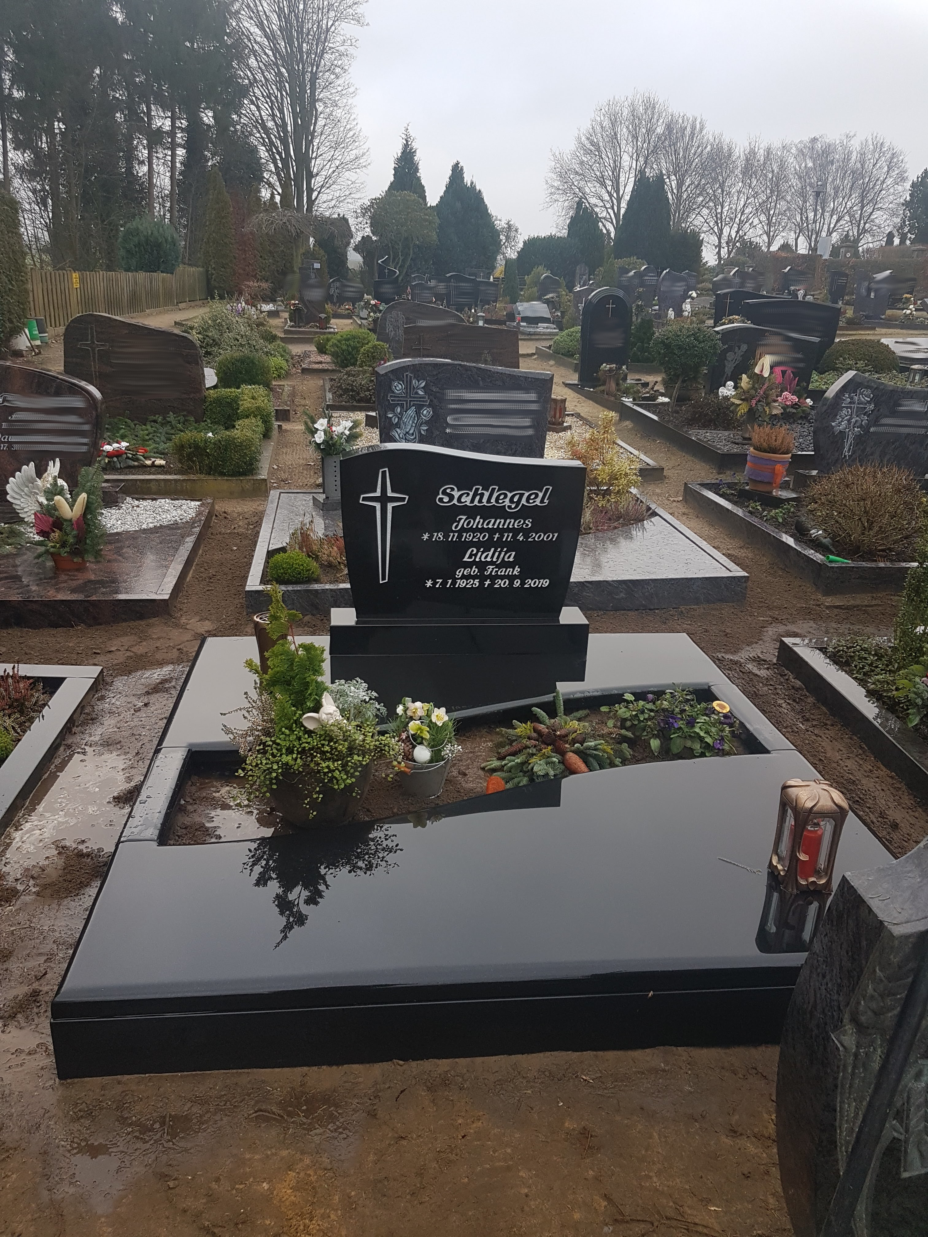 Ein schwarzer Grabstein mit Blumen, Kerze und weißer Gravur auf einem Friedhof