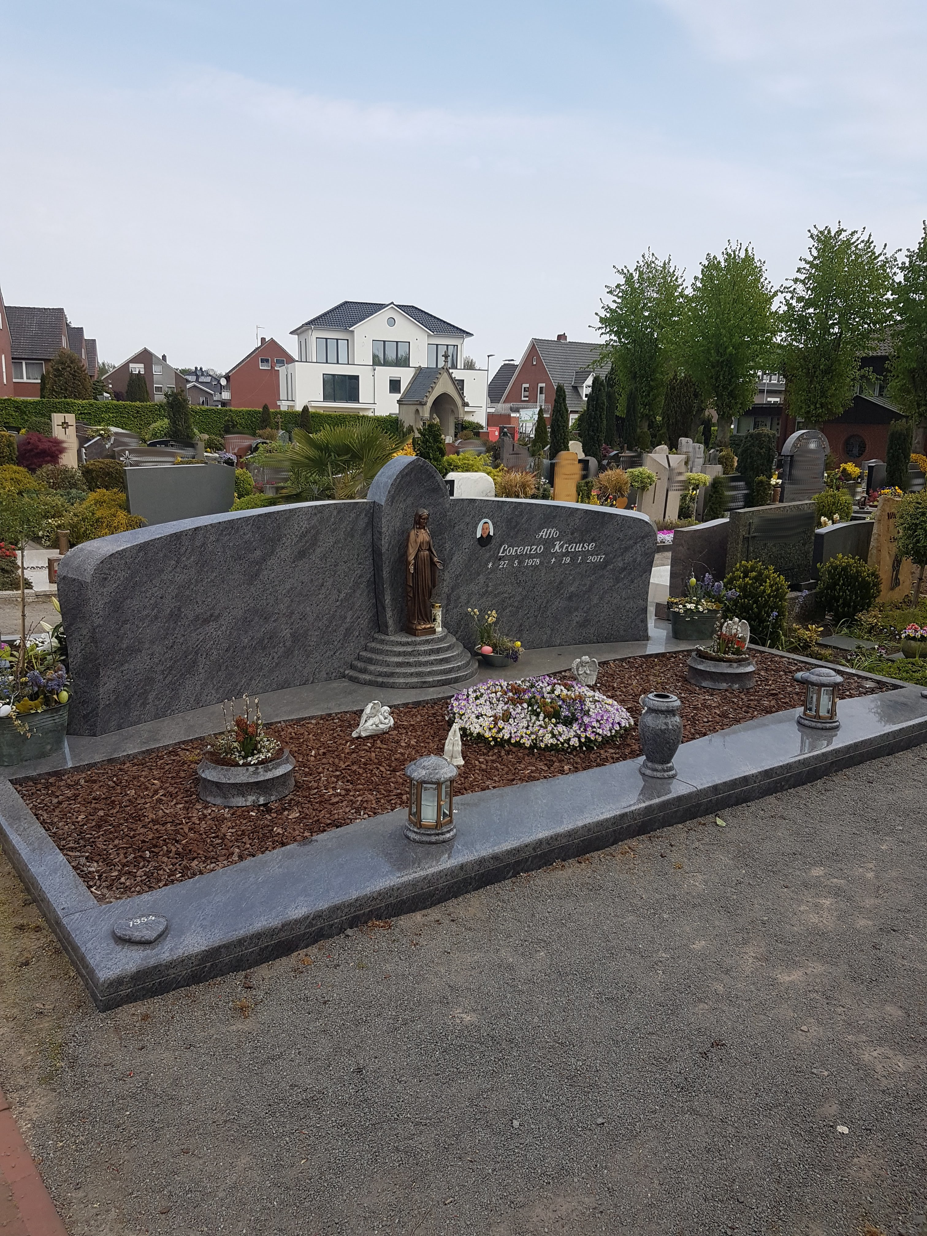 Ein großes, gepflegtes Grab mit grauem Stein, einer Statue und bunten Blumen