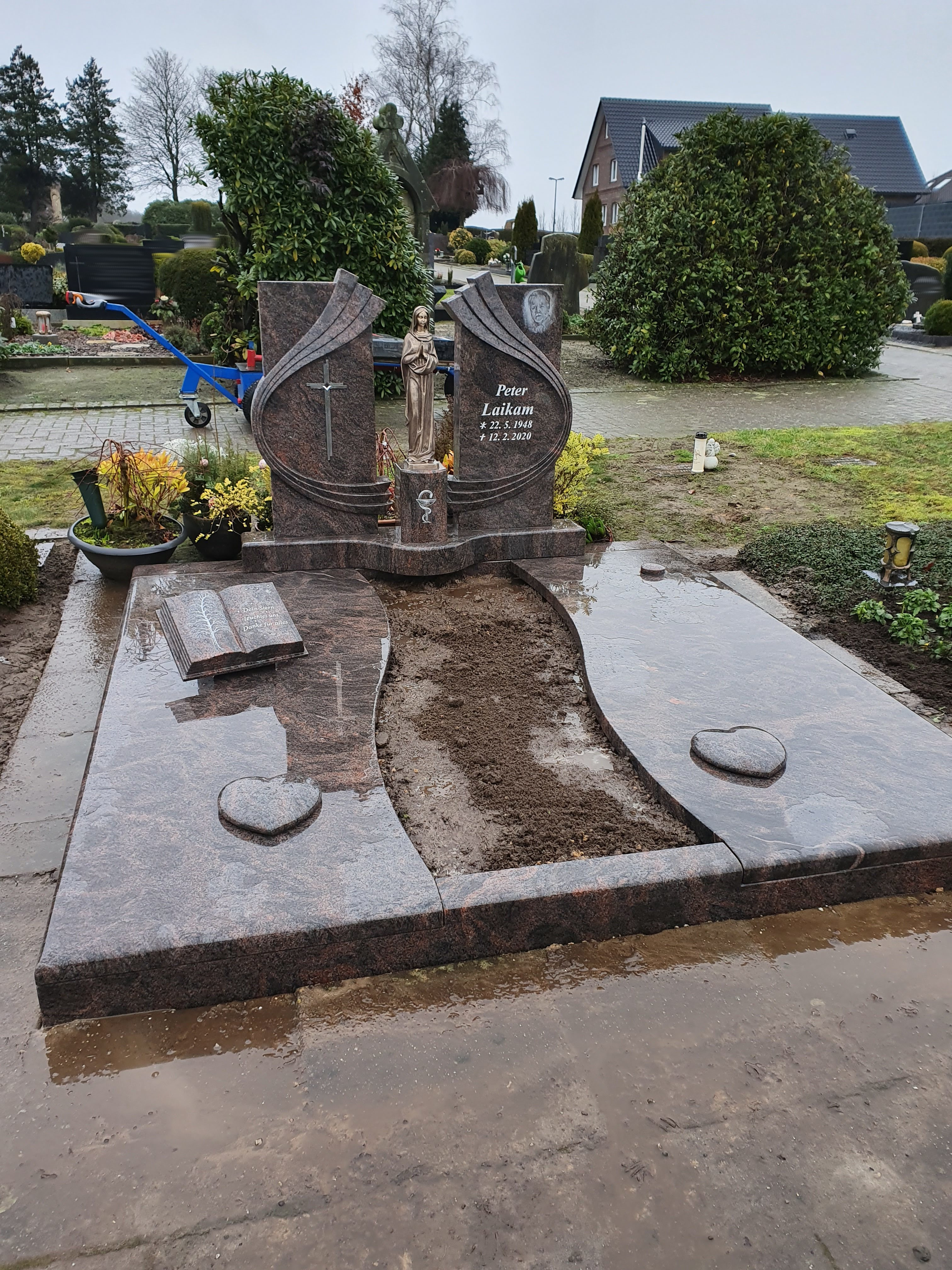 Grabstein aus braunem Marmor mit Statue und frischem Erdreich in der Mitte