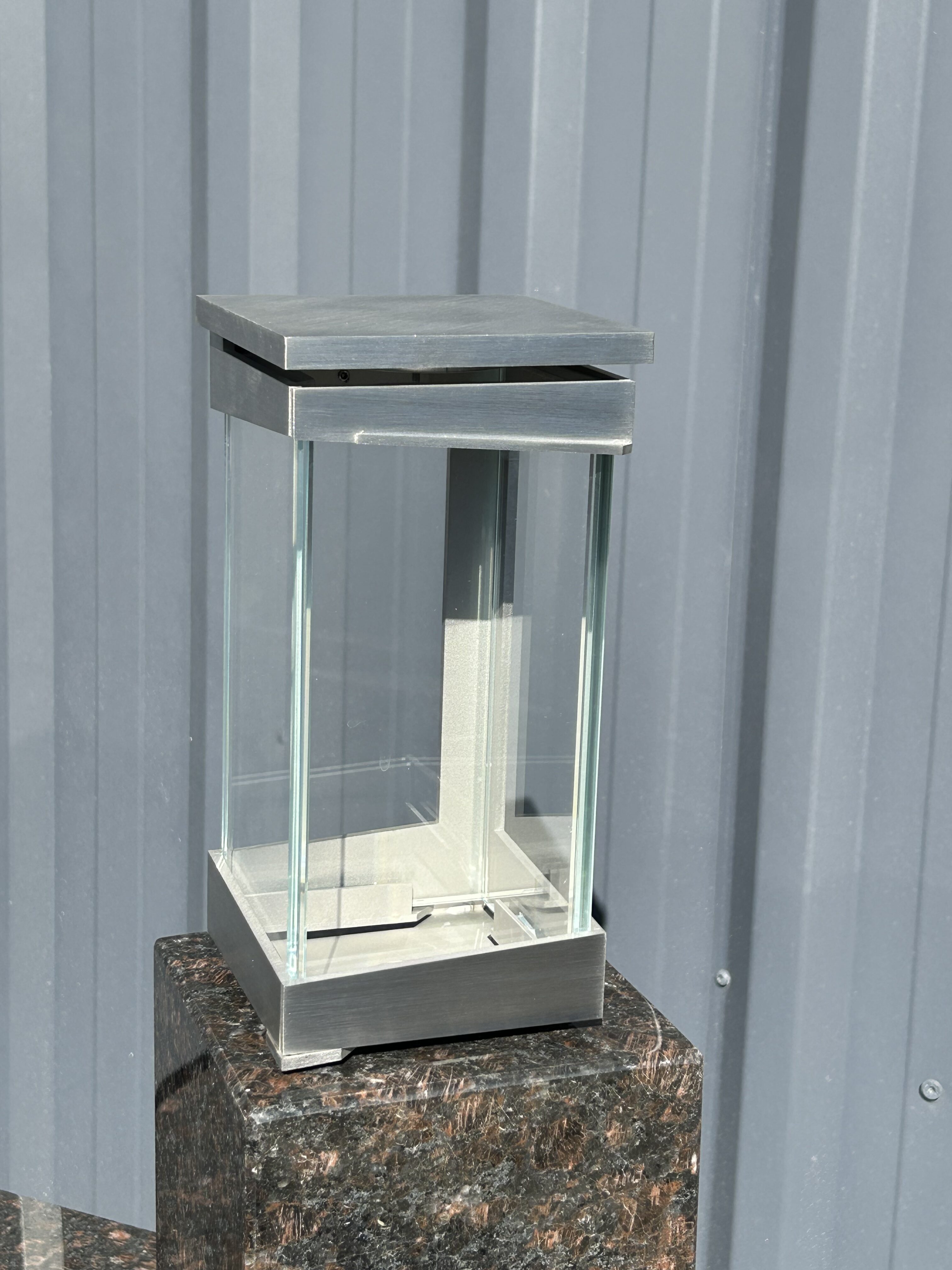 Eine moderne Laterne aus Glas und silberfarbenem Metall steht auf einem Marmorsockel