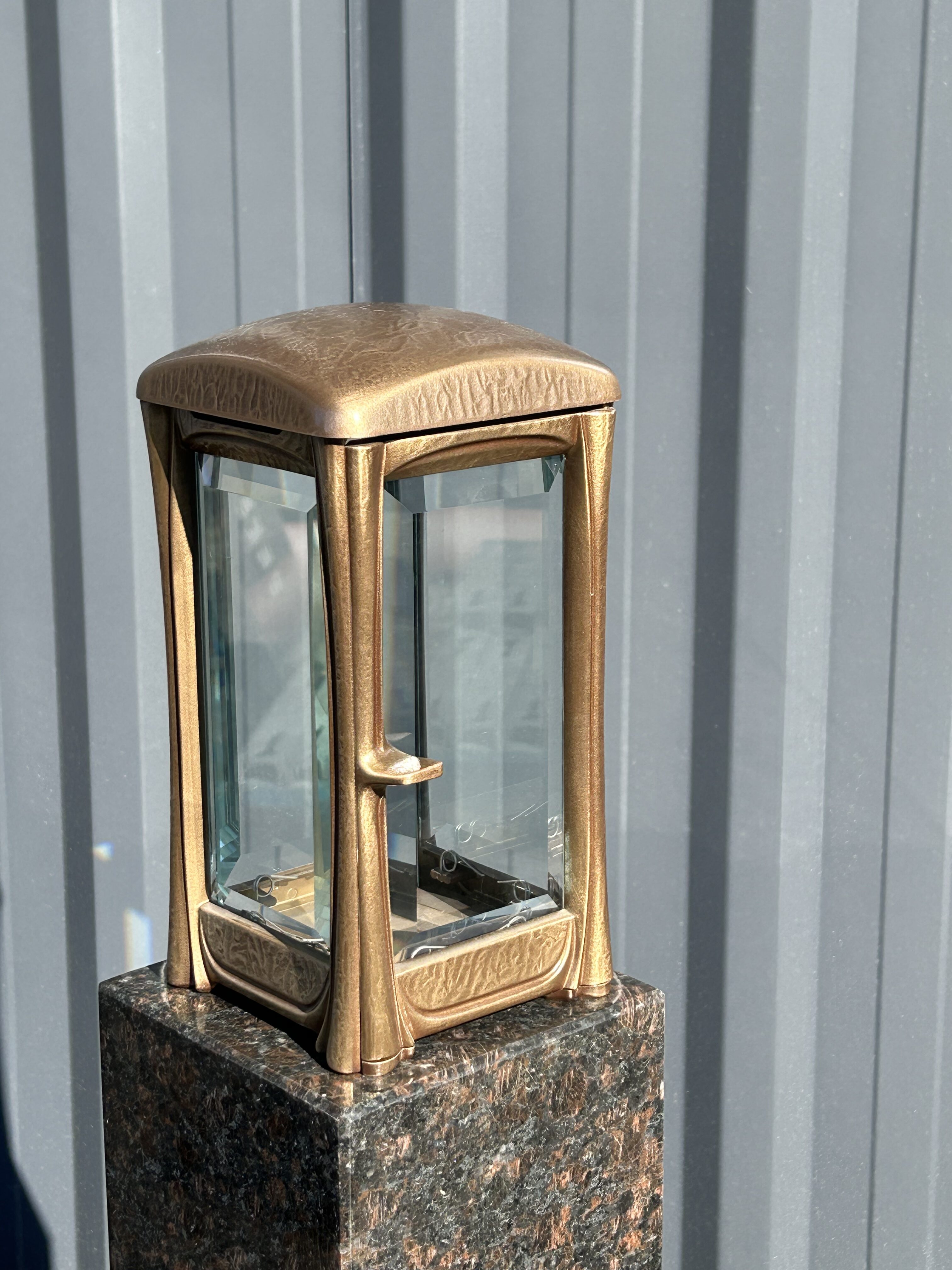 Eine bronzefarbene Laterne mit klarem Glas steht auf einem polierten Steinsockel