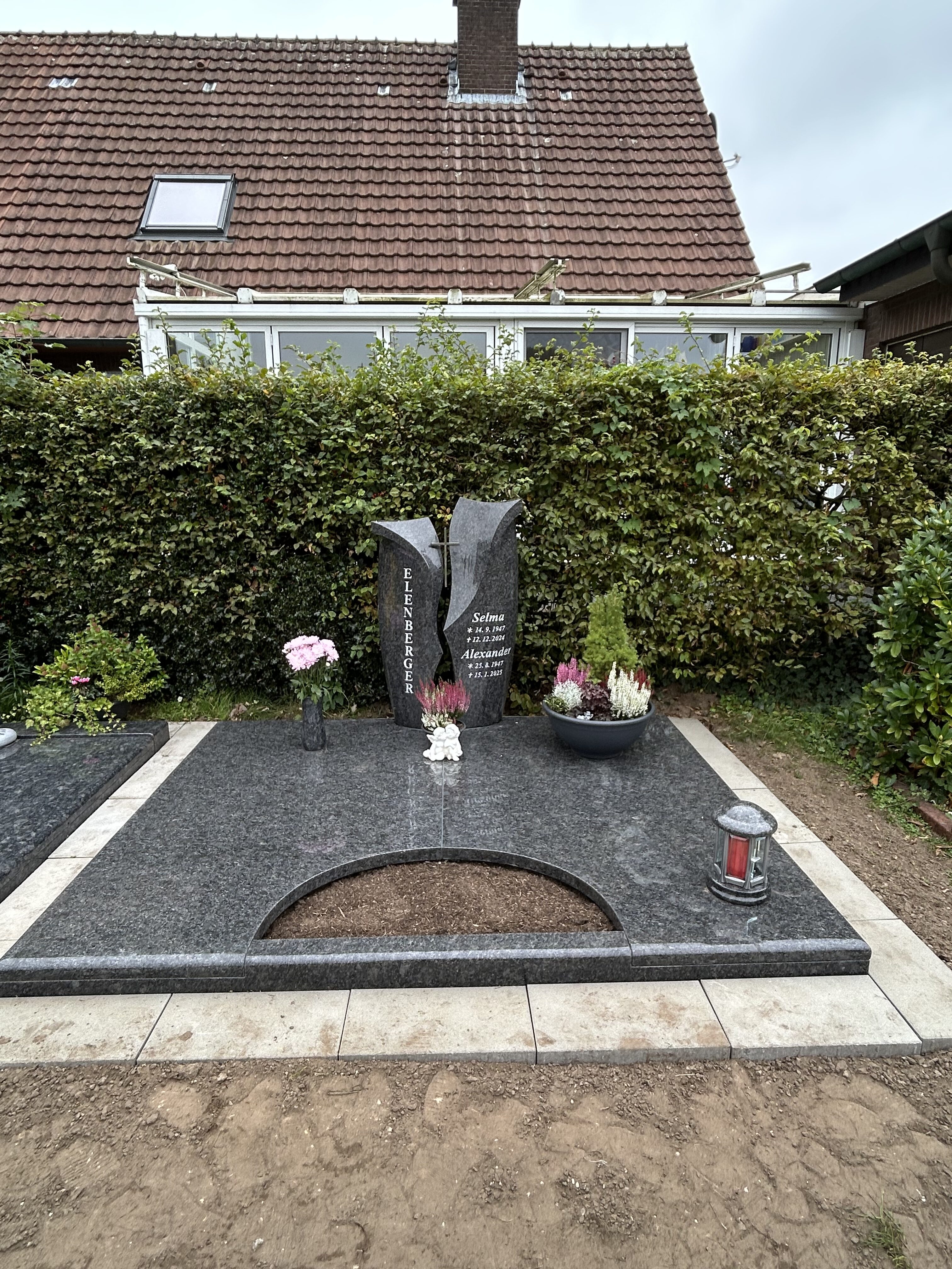 Grabstein aus dunklem Granit mit Blumen und rotem Licht auf gepflegtem Grabfeld