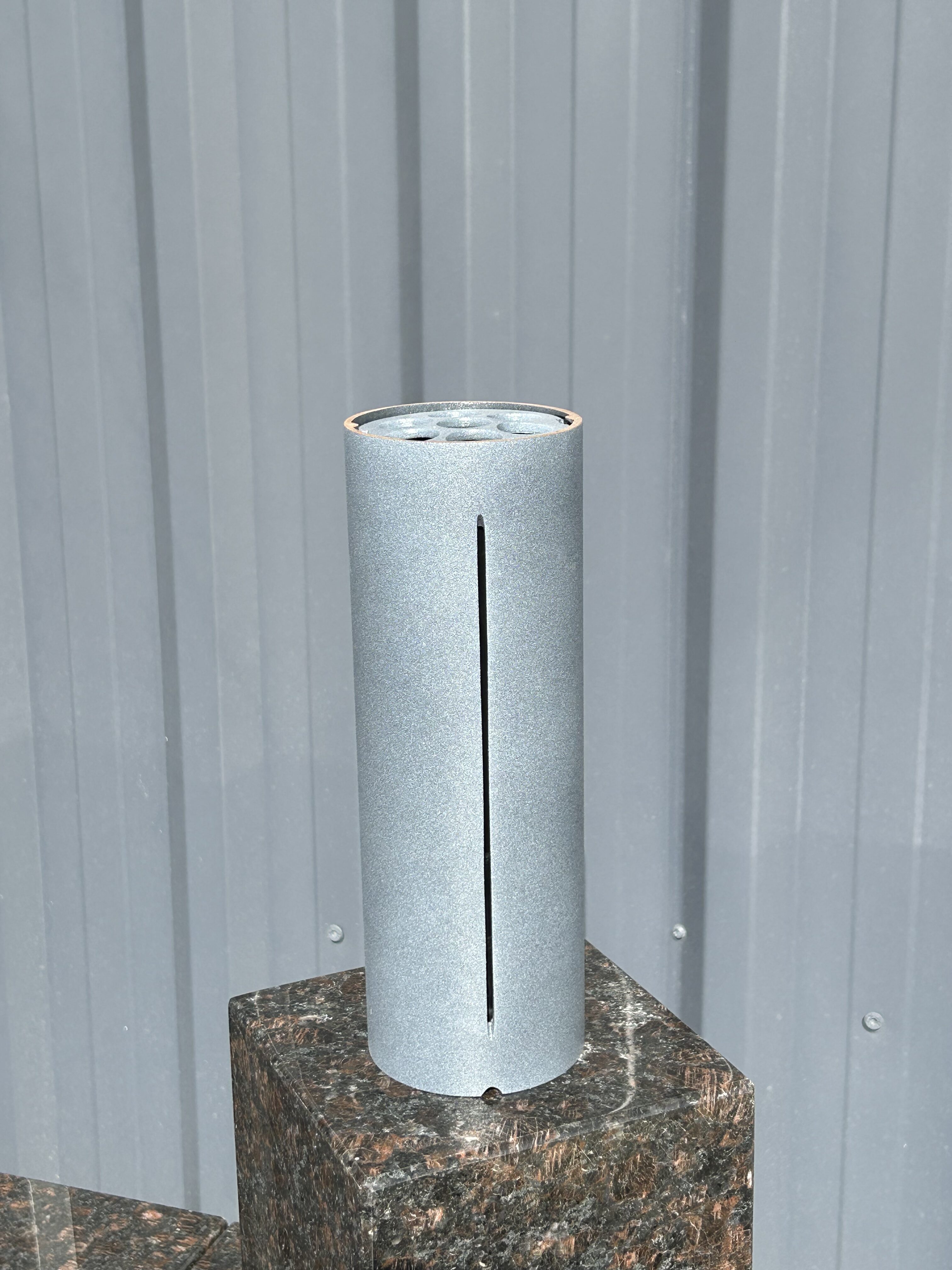 Ein silberner zylindrischer Behälter mit Schlitz steht auf einem dunklen Steinquader