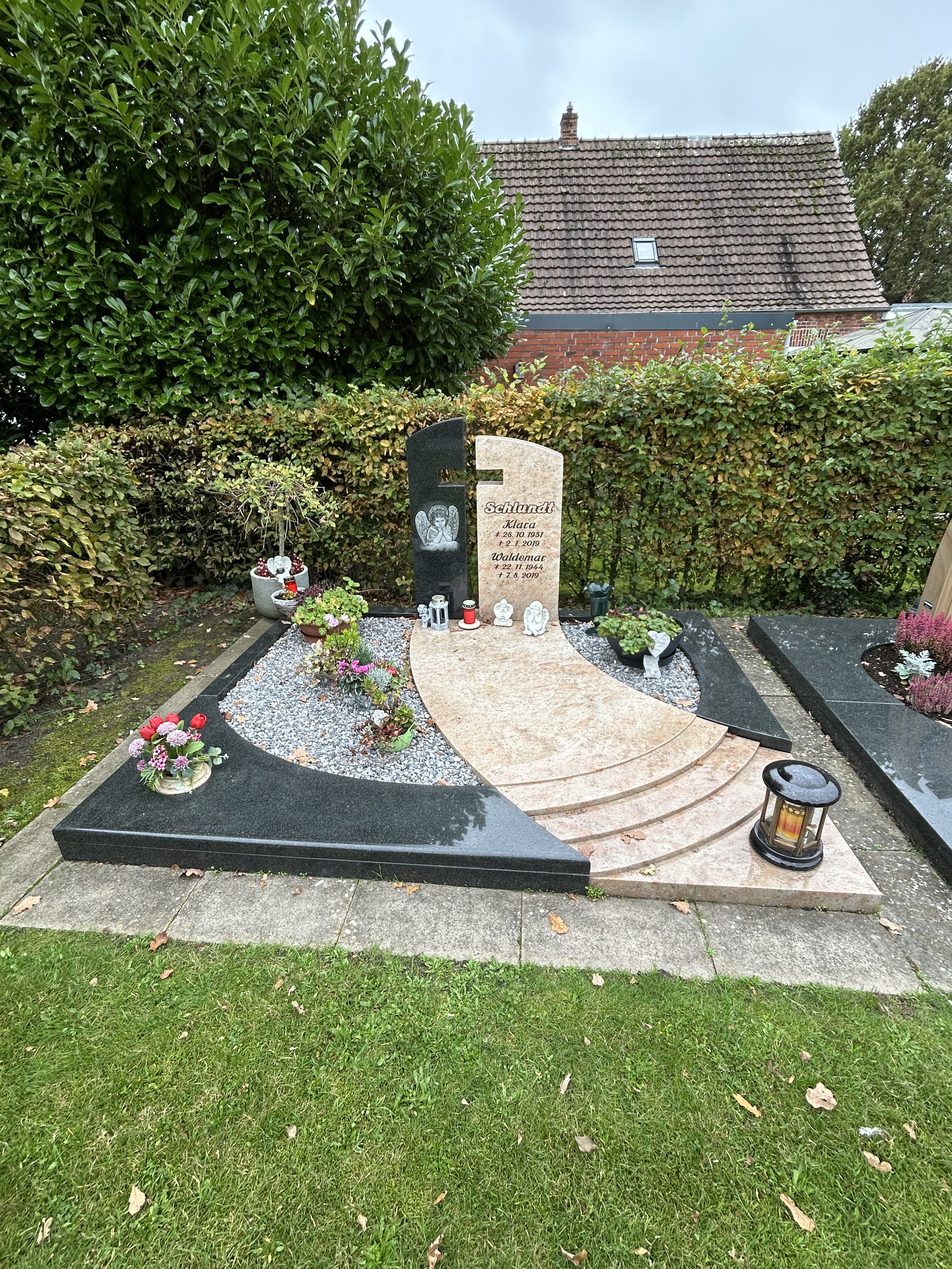 Ein gepflegtes Grab mit zwei Grabsteinen, Blumen, Kieselsteinen und einer Laterne