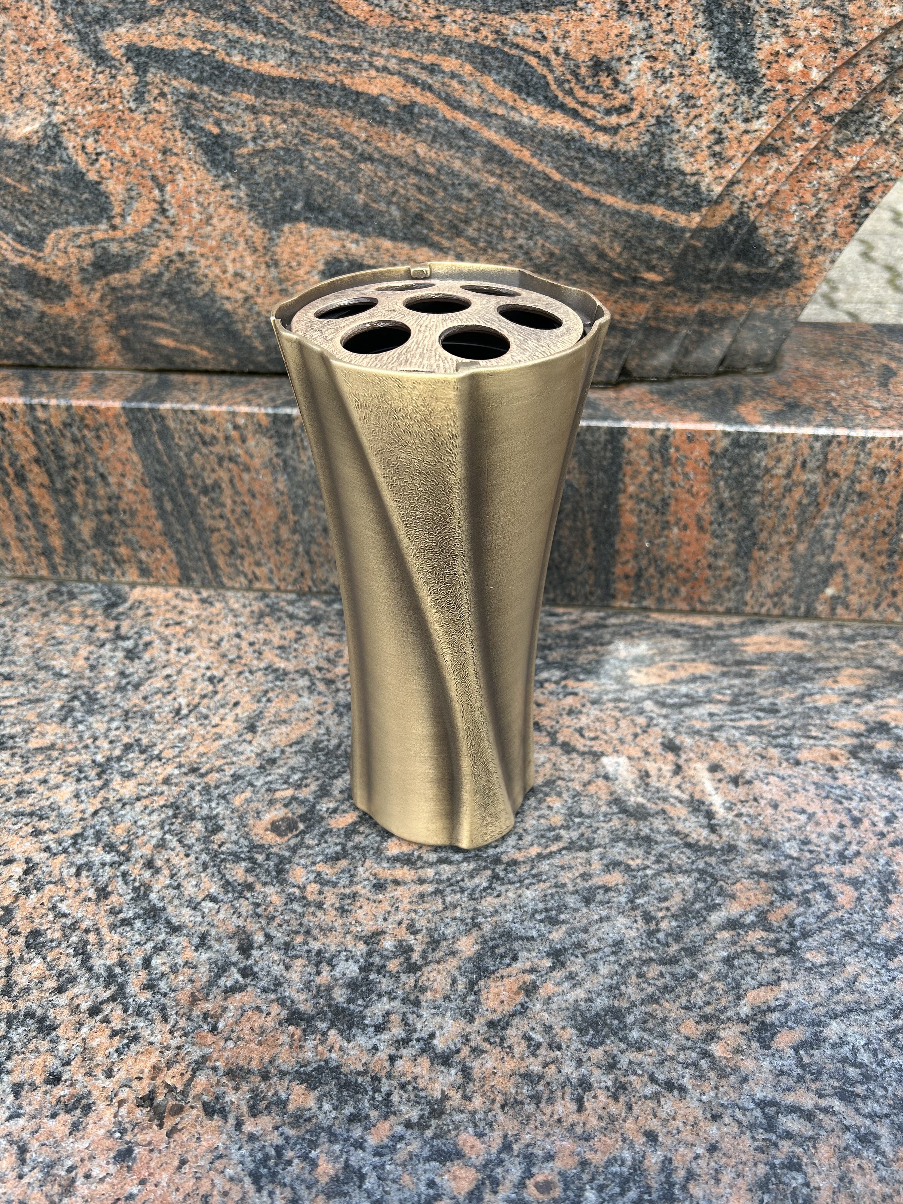 Eine bronzefarbene Vase mit sechs Öffnungen steht auf einem marmorierten Grabstein
