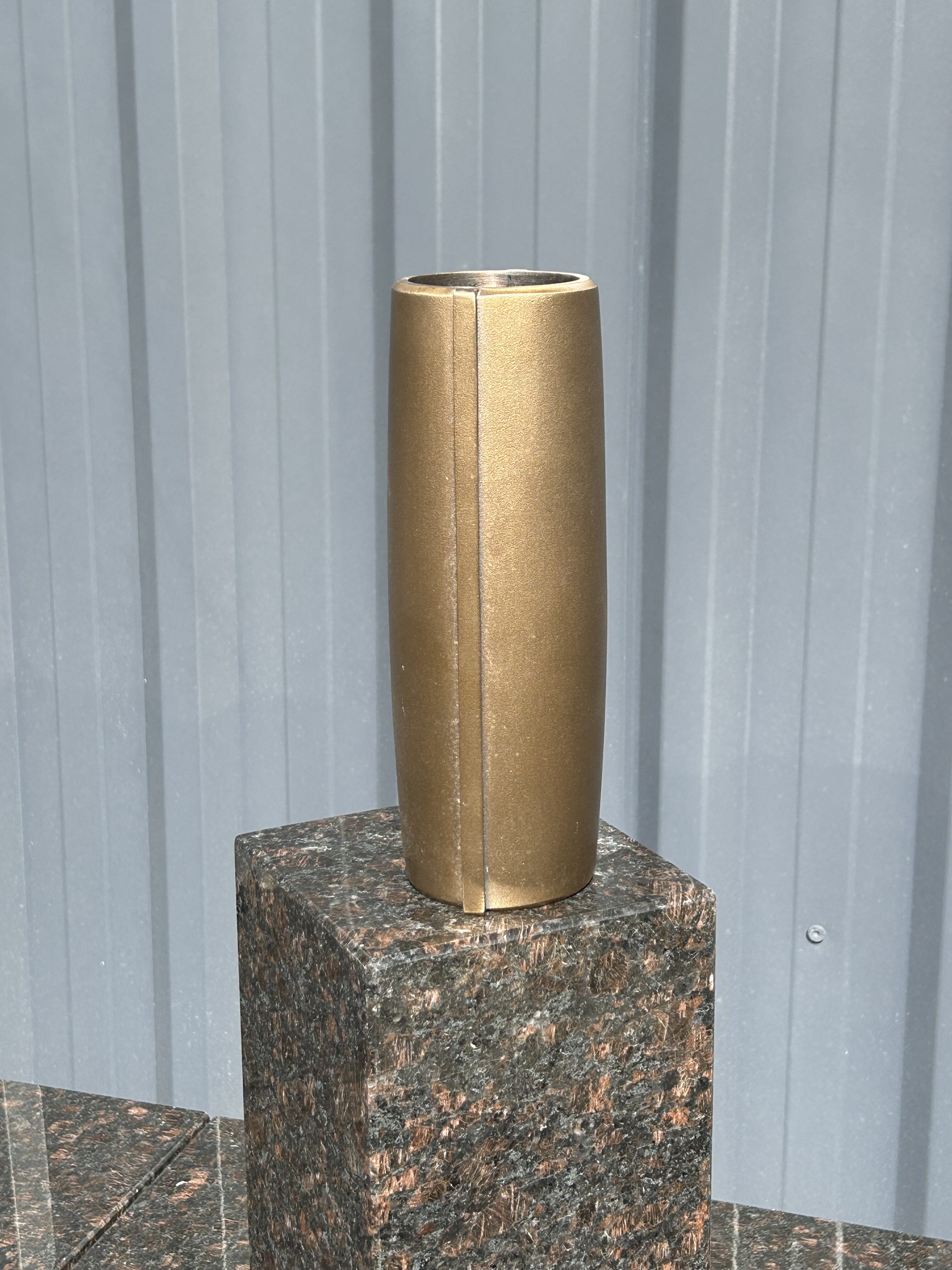 Eine goldene, zylindrische Vase steht auf einem glänzenden dunkelroten Marmorsockel