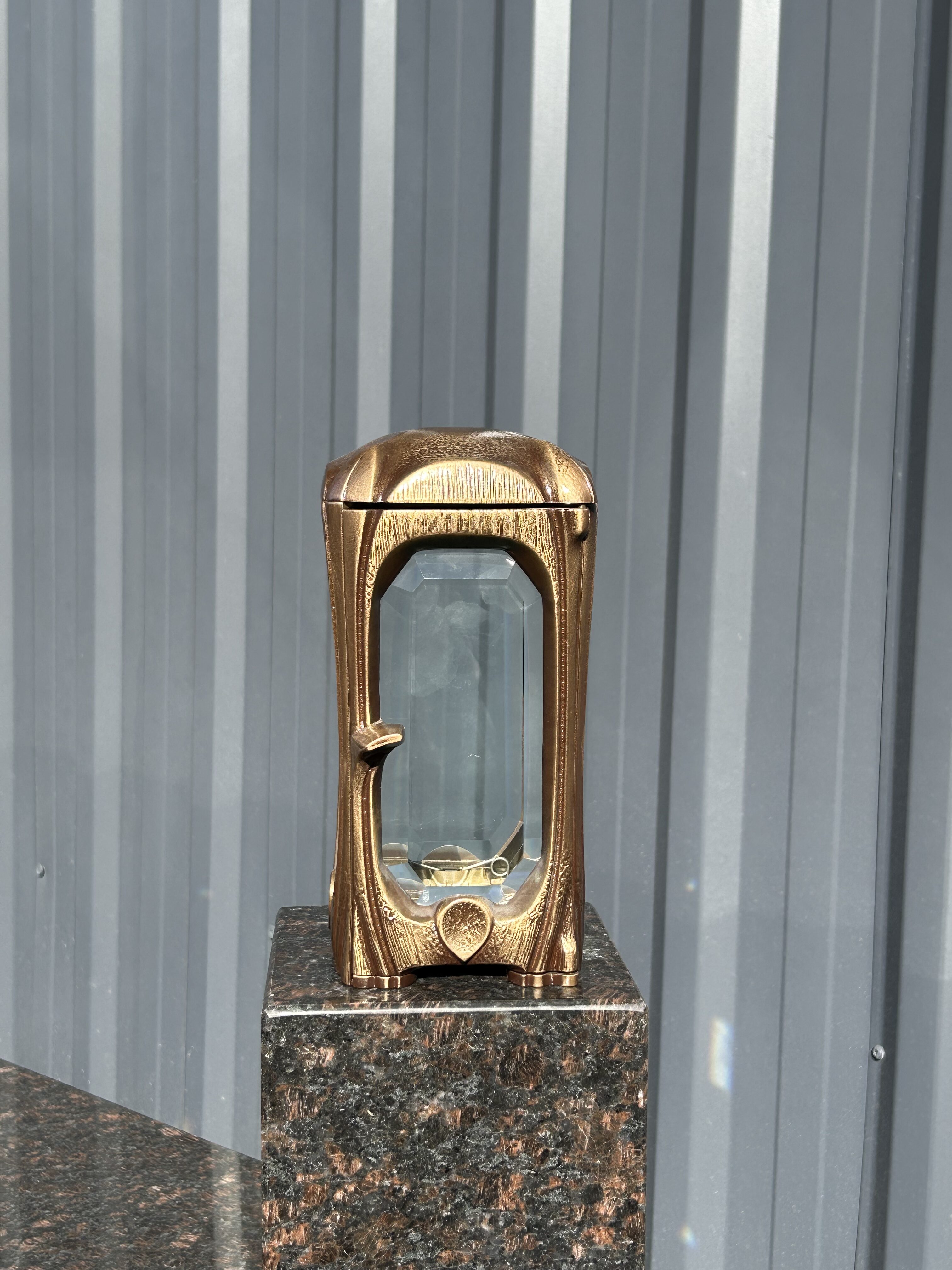 Eine goldene Laterne mit Glasfenstern steht auf einem polierten Marmorsockel im Sonnenlicht