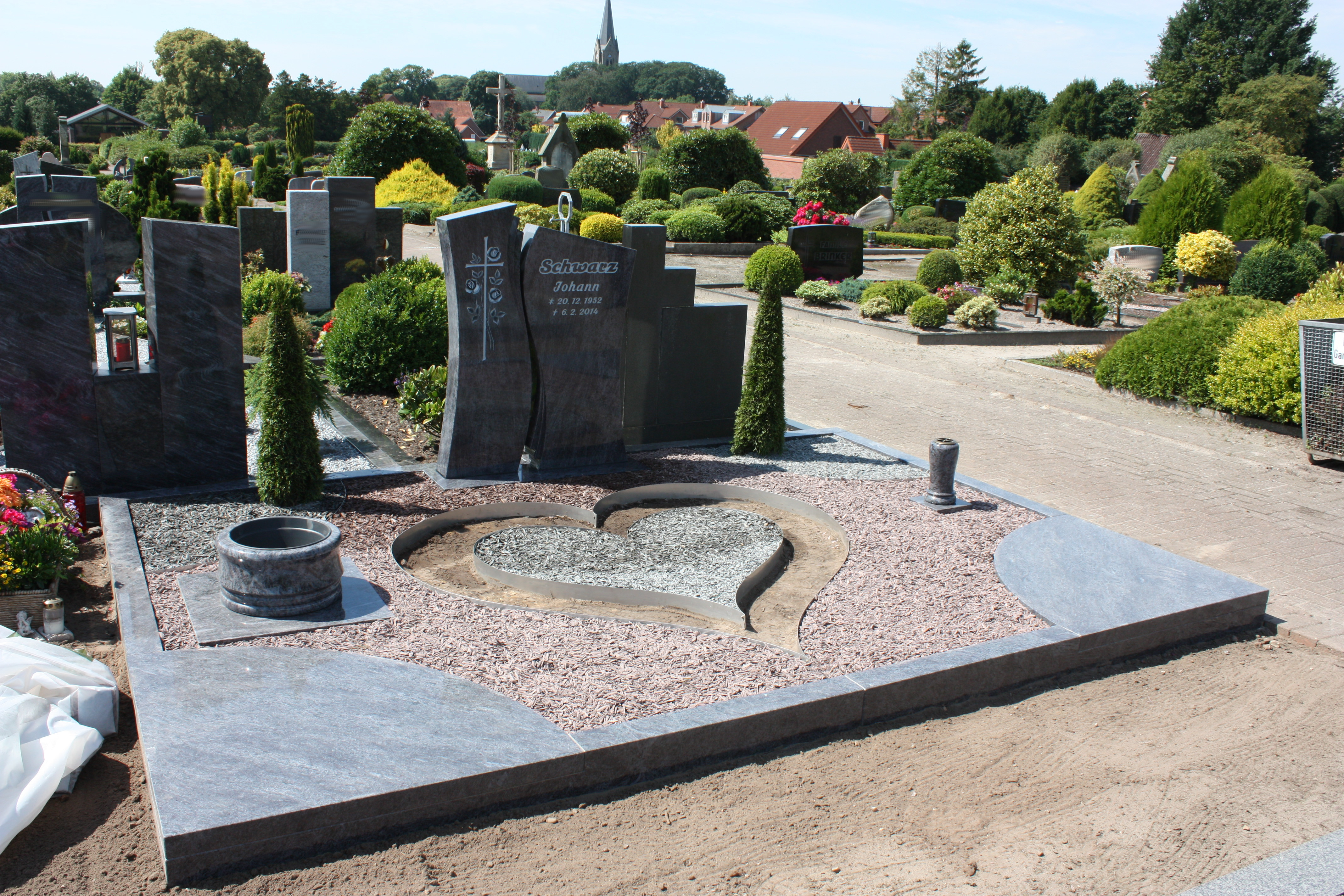 Ein kunstvoll gestaltetes Grabmal mit Herzform, grauen Steinen und grüner Bepflanzung