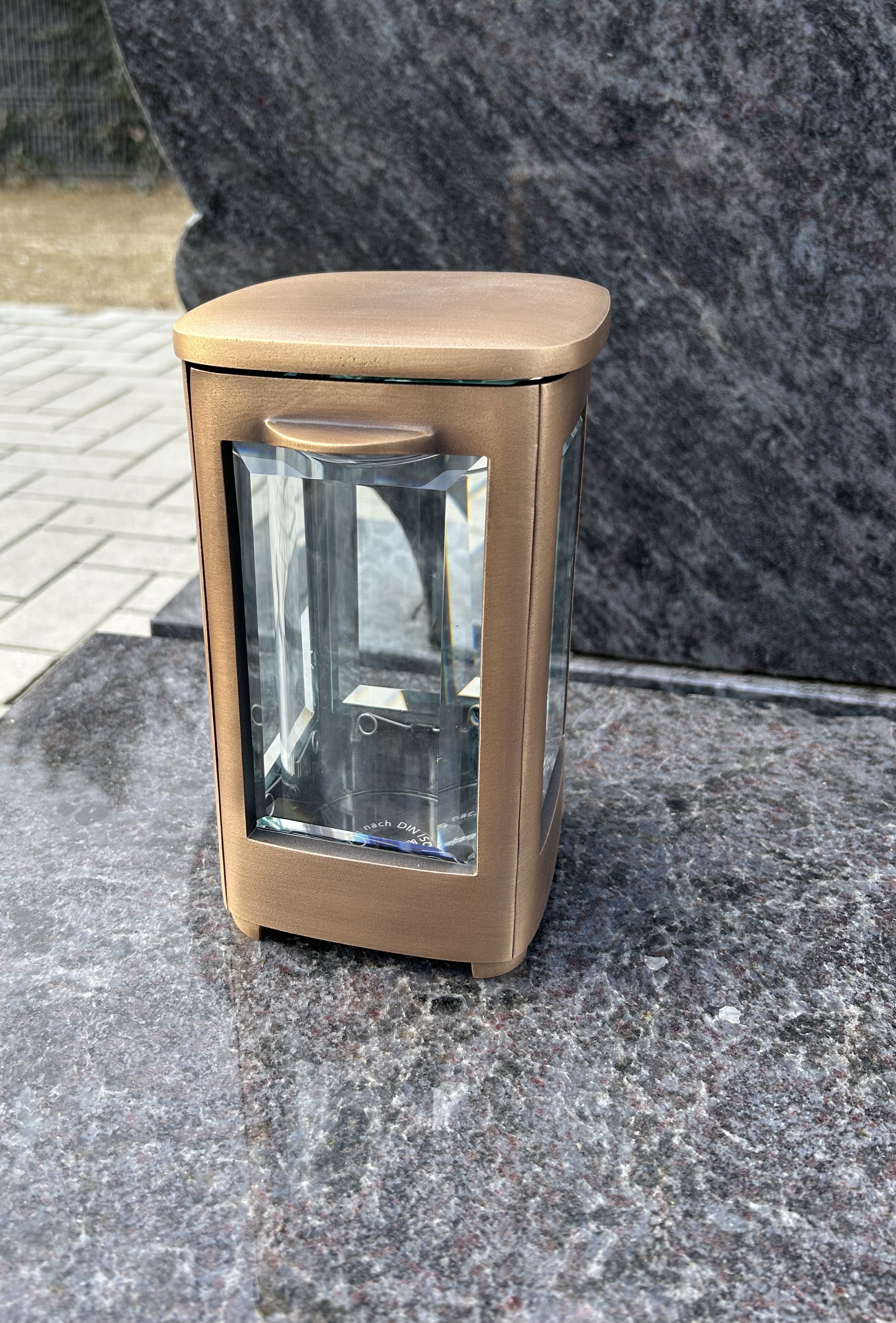 Eine bronzefarbene Laterne mit Glaseinsätzen steht auf einer polierten Steinplatte