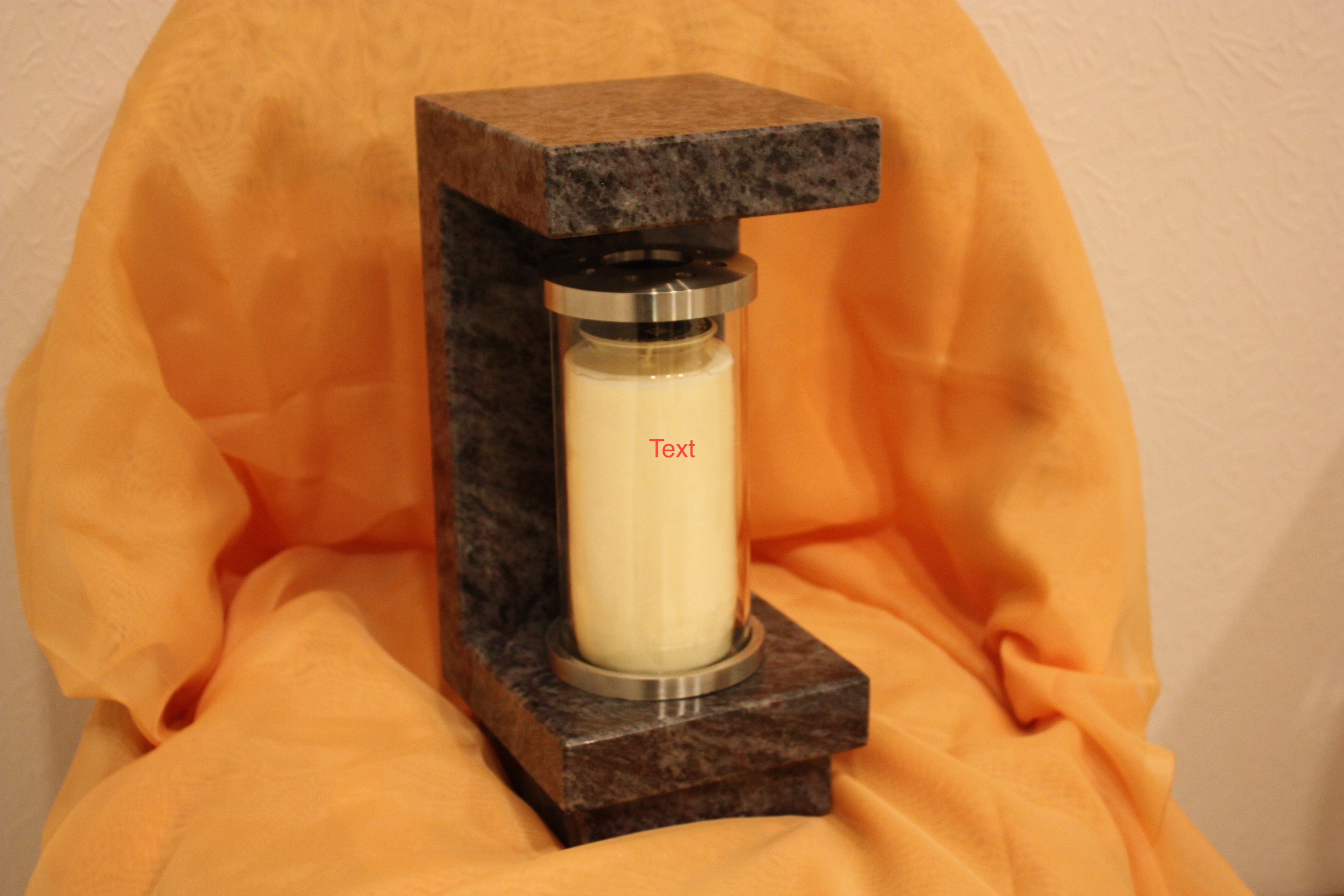 Eine cremefarbene Kerze steht in einem modernen Halter aus dunklem Stein vor gelbem Stoff