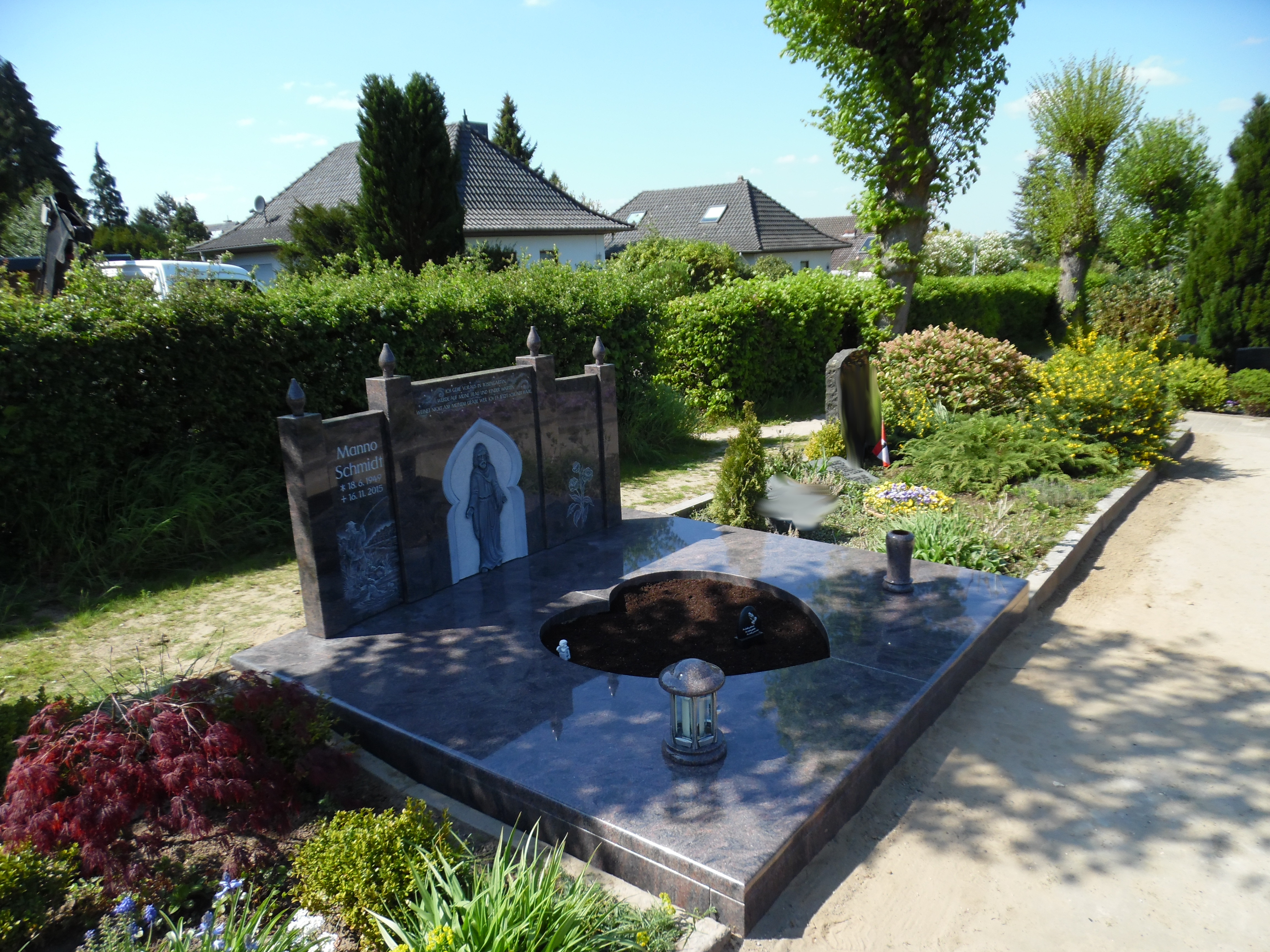 Ein gepflegtes Grab mit dunklem Stein, Gravur einer Frau und vielen grünen Pflanzen