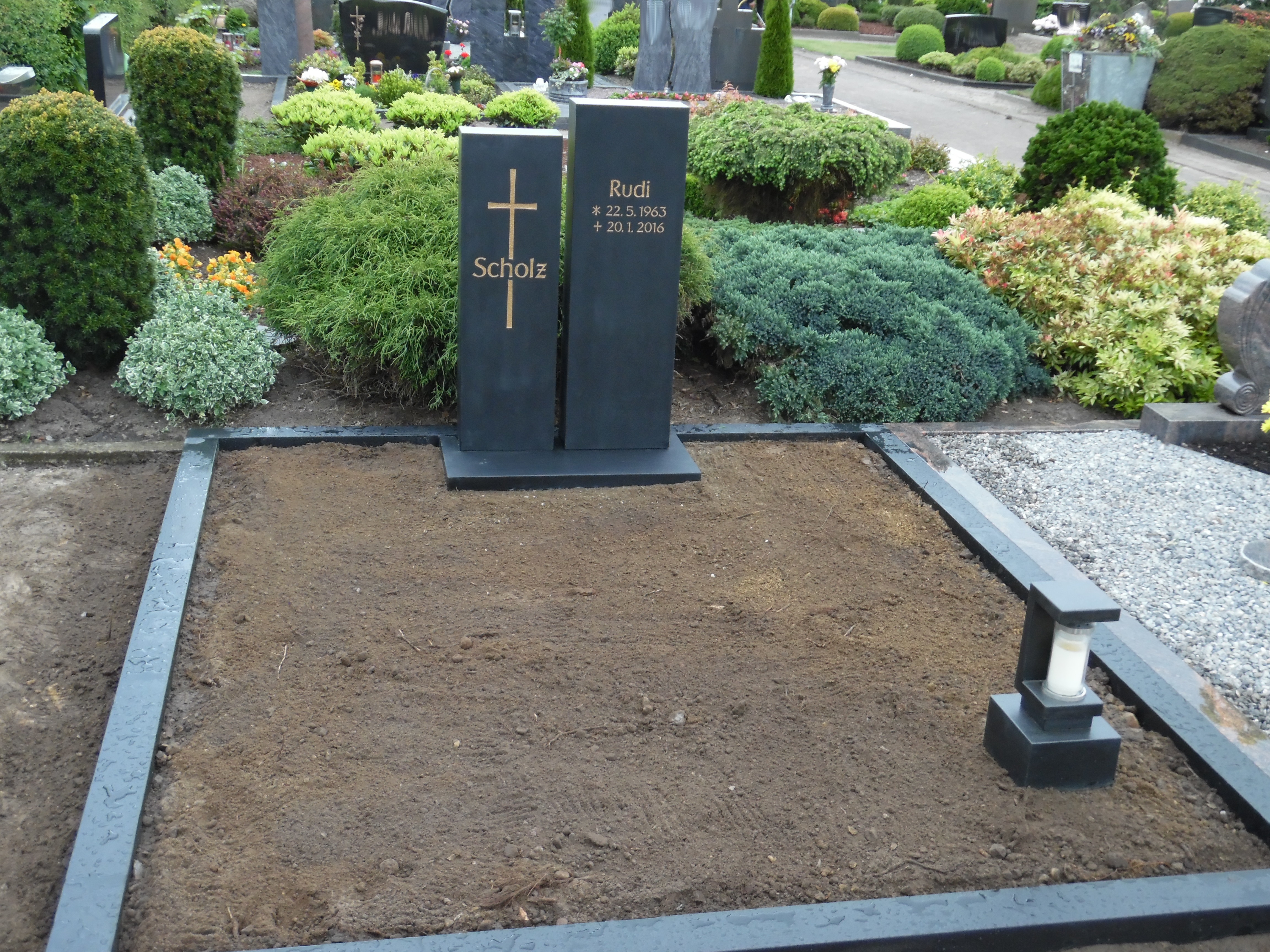 Ein schwarzer Grabstein mit goldener Schrift steht auf einem frisch bepflanzten Grab