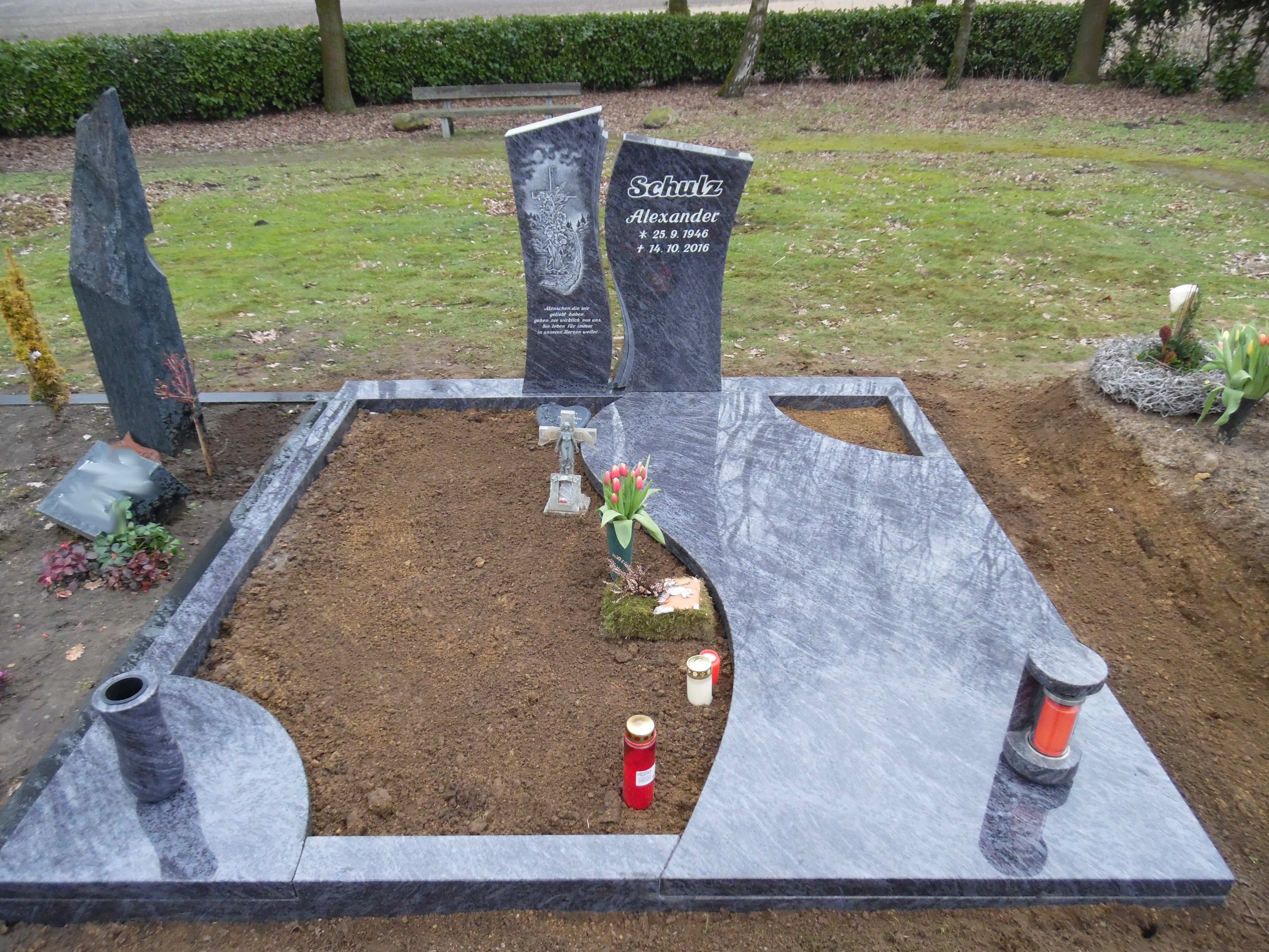 Ein modernes graues Grabmal mit Blumen, Kerzen und dem Namen Alexander Schatz