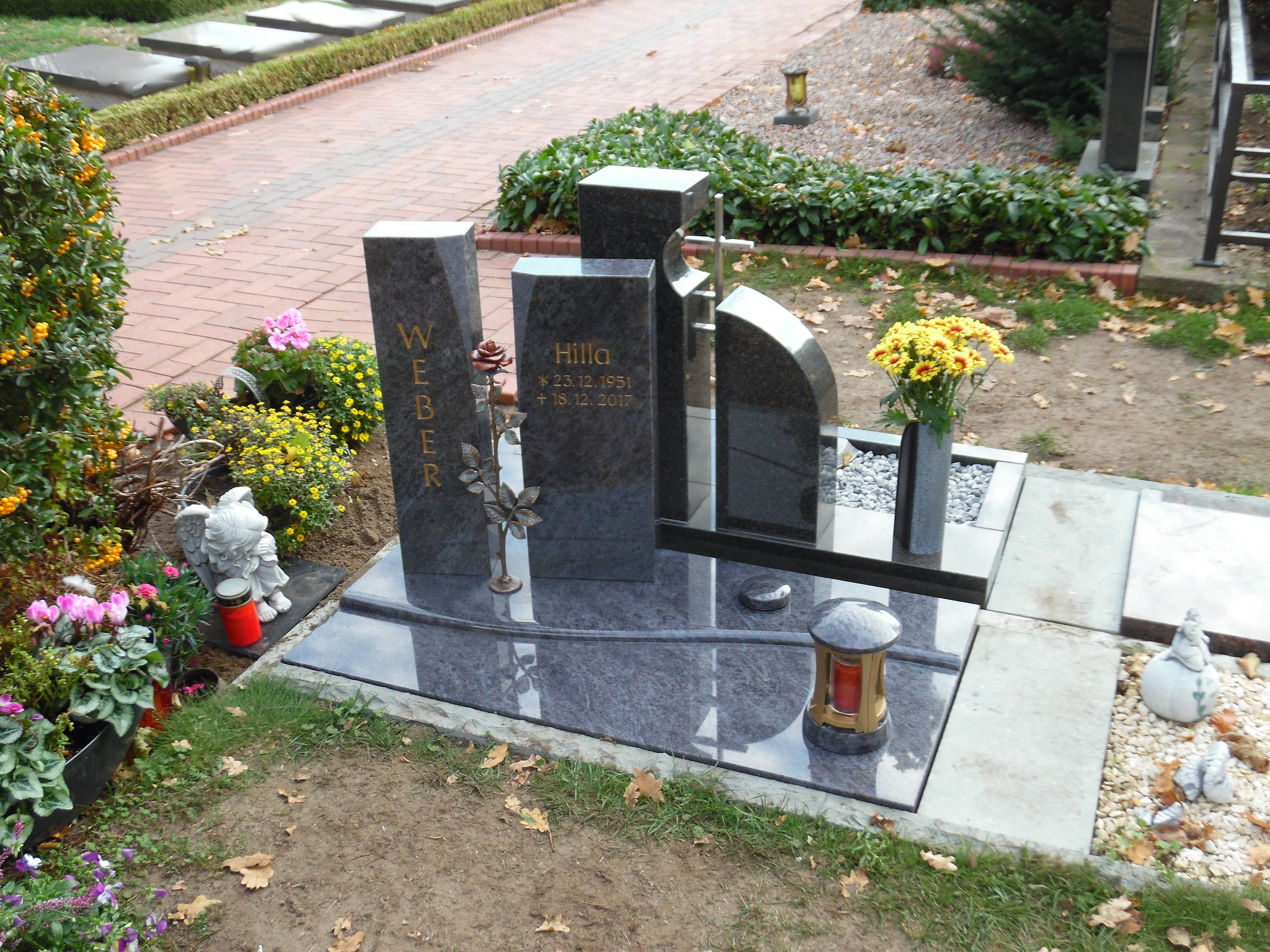 Ein stilvoller schwarzer Grabstein mit goldener Inschrift umgeben von bunten Blumen und Dekorationen