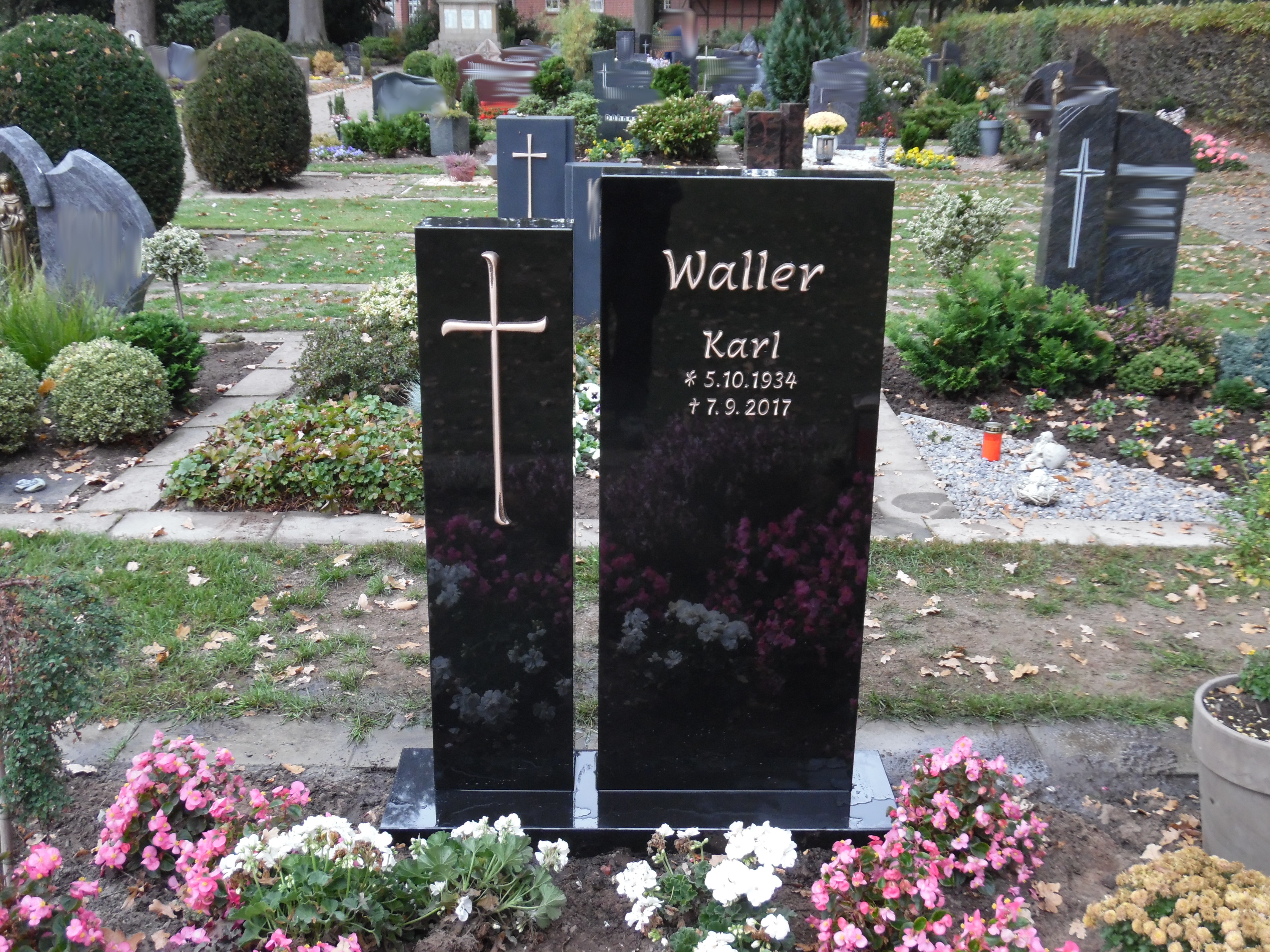 Ein schwarzer Grabstein mit Kreuz und goldener Inschrift steht auf einem Friedhof