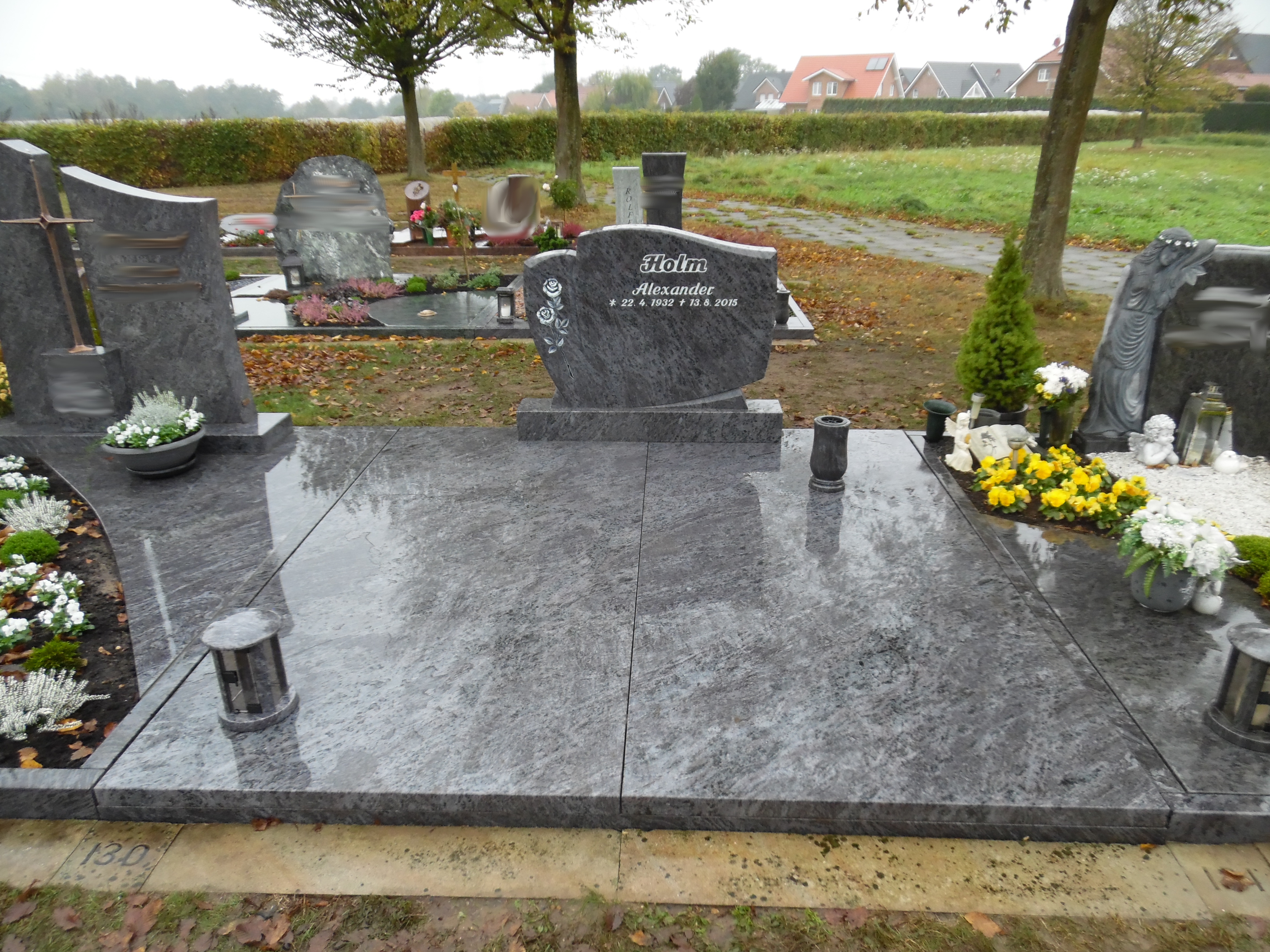 Ein gepflegtes graues Grab mit Blumen, Kerzen und einem verzierten Grabstein